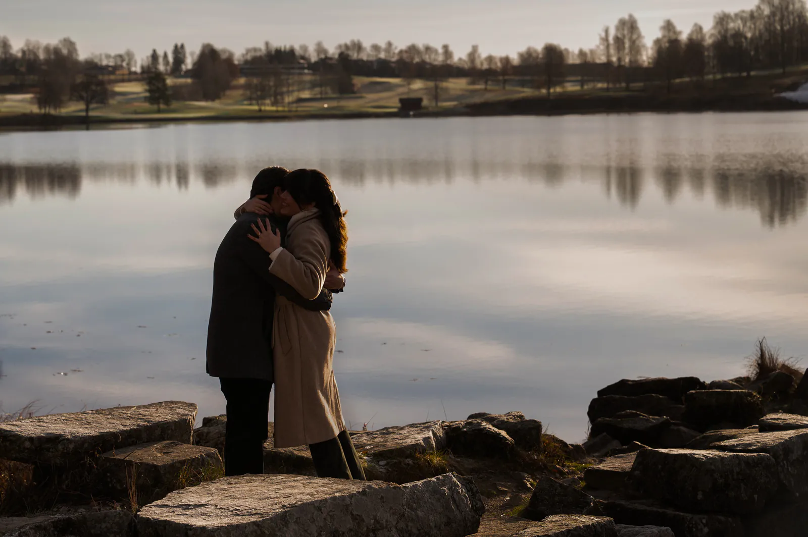 Paulina y Alejandro abrazados frente a un lago al atardecer